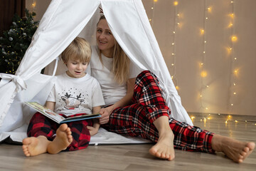 barefoot mother and son in pajamas sit in a play tent in the room and read a book. Cozy atmosphere....