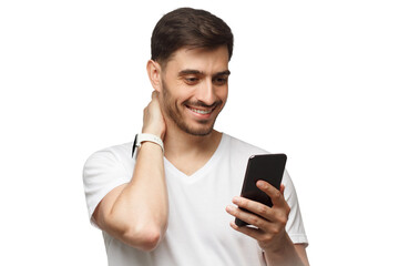 Young man wearing white t-shirt, holding phone in hand and looking at app on screen with smile