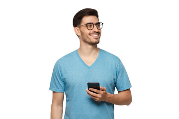 Young aspired man standing in blue t-shirt holding phone in hand and looking away with dreamful smile