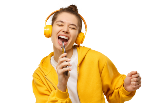 Young woman in yellow hoodie and wireless headphones, singing with closed eyes, holding phone as microphone