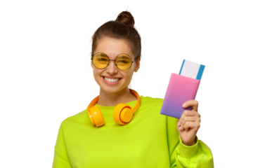 Happy smiling female wearing neon green top, glasses and wireless headphones around neck, holding passport with airplane tickets