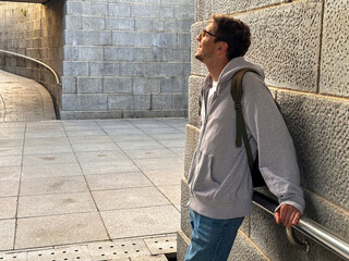 Man in gray hoodie leans thoughtfully against a concrete wall in a modern space