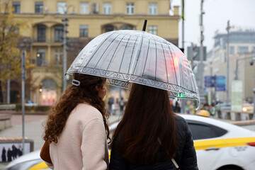 Two women with one umbrella standing on a street in front of taxi car. Rain in autumn city