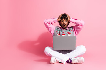 Full size photo of nice young man hands touch head laptop empty space wear christmas vest isolated on pink color background