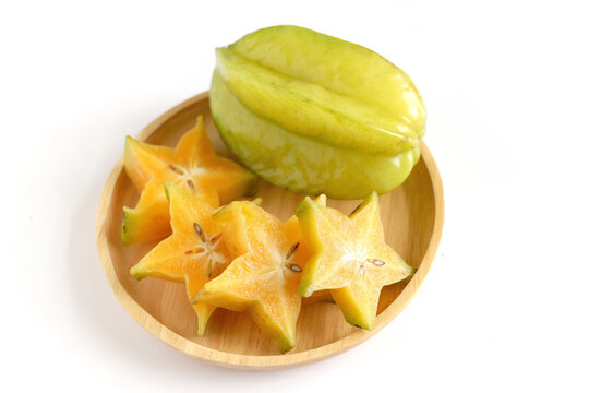 Two ripe juicy carambola starfruit whole with slice in wooden plate on a white background. Averrhoa carambola, star apple, delicious tropical fruit.