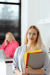 A woman wearing glasses and holding a stack of papers