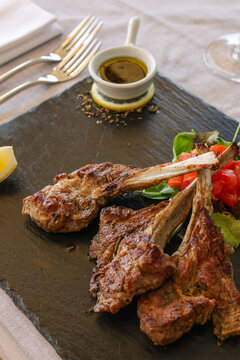 Costolette di agnello cotte sulla brace e servite con insalata di pomodori di contorno e salsa alle erbe