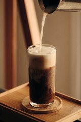milk falling into a glass of coffee at dawn at home