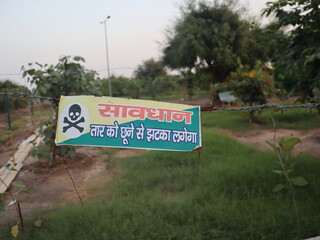 A caution sign in Hindi warns against touching a barbed wire fence, indicating the risk of electric...