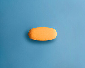 Close up of yellow pill on blue background, top view.