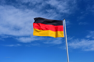 The flag of Germany flutters in the wind against a blue cloudless sky