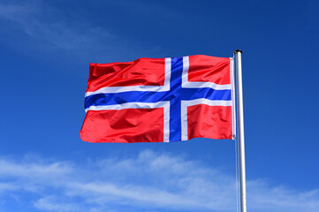 The flag of Norway flutters in the wind against a blue cloudless sky