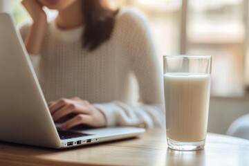 Fototapeta premium Woman working on laptop while enjoying a glass of fresh milk in a cozy setting