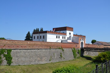 Fototapeta premium The photo shows Dubno Castle in Ukraine. The structure, adorned with decorative patterns, rises above lush greenery under a clear sky.
