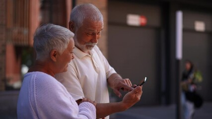 Closeup of cheerful elderly couple happily exploring new city streets, relying on smartphone for directions. Gray-haired senior male and female navigating unfamiliar city with smartphone navigation. - Powered by Adobe