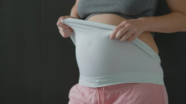 Pregnant bliss: Mom-to-be embraces her baby bump with a soft fabric bandage, providing gentle support. Maternity made comfortable. Slowmotion video