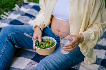 Pregnant woman having lunch and holding a bowl with salad in hands