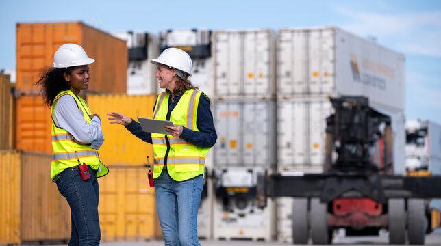 Engineer or dockworker working in the construction container dock yard checking and inspection containers data on computer program environment is container shipping Logistics business concept.