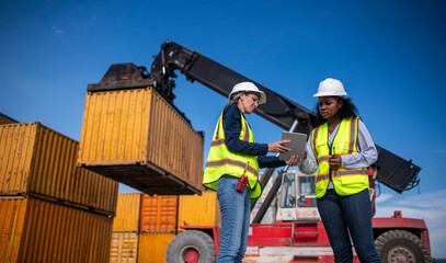 Engineer or dockworker working in the construction container dock yard checking and inspection containers data on computer program environment is container shipping Logistics business concept.