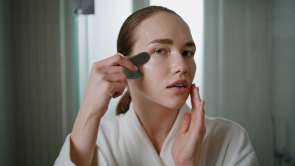 Young woman massaging face with gua sha. Closeup girl do stone treatment at home