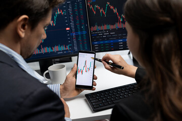 Focusing on phone with discussing dynamic stock market in two business traders online website compare with pc screens in real time currency rate investment on risk data at modern office. Postulate.