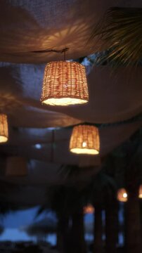 Woven lantern chandeliers at tropical beach during evening.