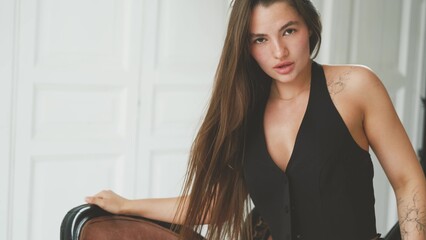 Portrait of young beautiful model posing in black lingerie and stockings on sofa in white room. Calm cute brunette in fashionable lingerie.