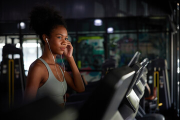 young sports woman working out with wired earbuds and running on treadmill in gym