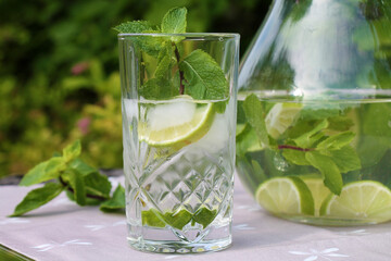 Clear drink with mint and lime in a tall glass in summer garden close-up.