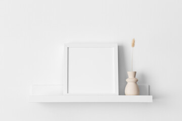 White square frame mockup with a lagurus decoration on the wall shelf.