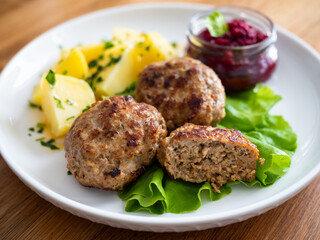Fried meatballs, boiled potatoes, beetroots and fresh vegetables served on white plate on wooden table
