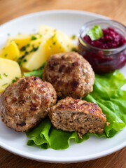 Fried meatballs, boiled potatoes, beetroots and fresh vegetables served on white plate on wooden table
