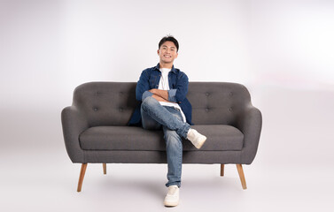 Full body image of young Asian man posing on sofa on white background