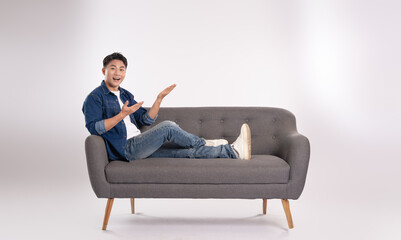 Full body image of young Asian man posing on sofa on white background
