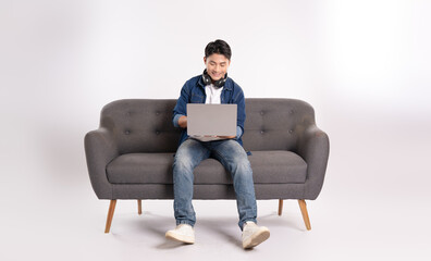 Full body image of young Asian man using laptop sitting on sofa on white background