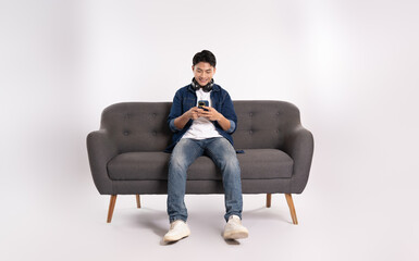 Full body image of young Asian man using phone sitting on sofa on white background