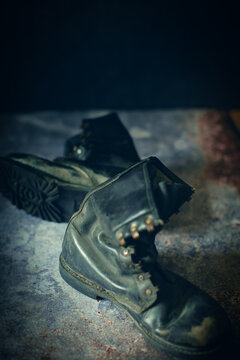 A pair of worn, dark leather boots lie on a mottled surface, casting soft shadows. The scene has a slightly vintage or nostalgic atmosphere, enhanced by the boots' rugged condition.