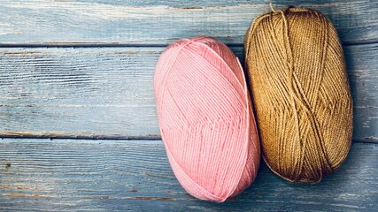 On a blue wooden background lie two skeins of acrylic threads of pink and beige colors. Top view. Handicraft. Copy space