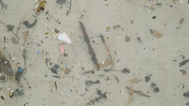 Ocean pollution. Close up of microplastic and debris floating in shallow water on sandy beach on Phuket island, Thailand. Garbage and trash in the sea. Environmental challenges and marine pollution