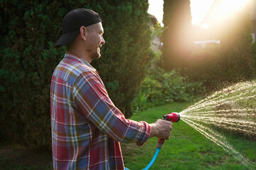 Man watering lawn with hose in backyard