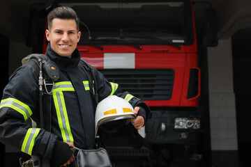 Fototapeta premium Portrait of firefighter in uniform with helmet near fire truck at station, space for text