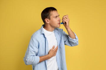 Man using asthma inhaler on yellow background