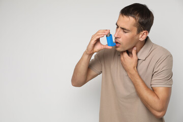 Man using asthma inhaler on light background, space for text