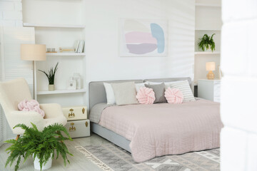 Large bed, houseplants and decorative elements in room. Stylish bedroom interior