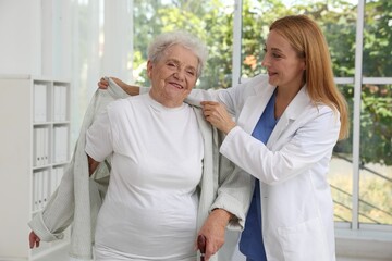 Obraz premium Healthcare worker helping senior patient to wear jacket in hospital