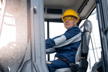 Naklejka premium Adult man builder in hardhat operate crane, driver of excavator working at construction site