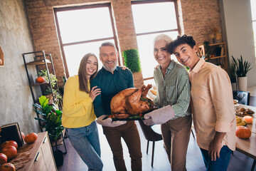 Photo of four friendly family members cuddle hold turkey celebrate thanksgiving dinner apartment...