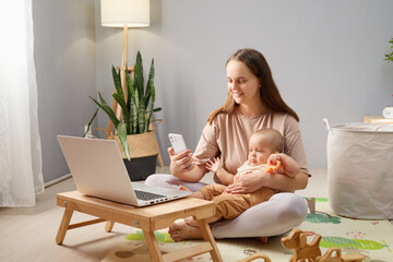 Hardworking businesswoman smiling while browsing internet on her cellphone and keeping eye on her...
