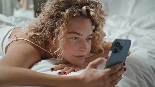 Restful woman using mobile phone lying in bed closeup. Serene girl scrolling