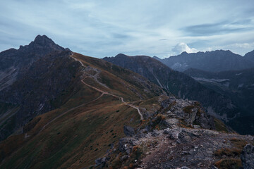 Fototapeta premium A narrow trail snakes through a mountainous terrain under a cloudy sky.